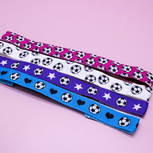 Four colorful ribbons with soccer ball, star, and heart patterns on a pink background.